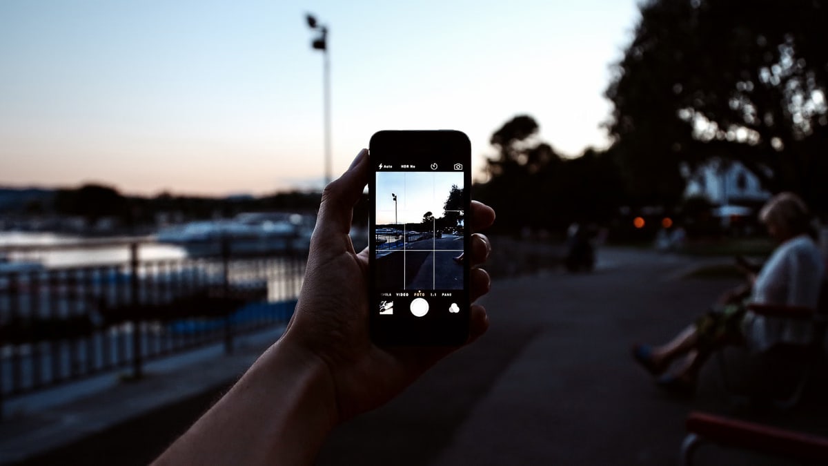 A hand holding a smartphone captures a serene evening park scene.